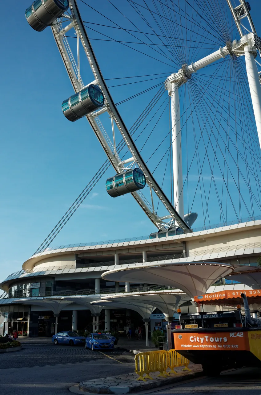 Capsules of the Singapore Flyer sweeping down toward the boarding terminal against a blue sky